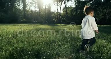 可爱的小男孩，穿着白衬衫在草地上奔跑。 动作缓慢。 4k. 婴儿后面的照相机。